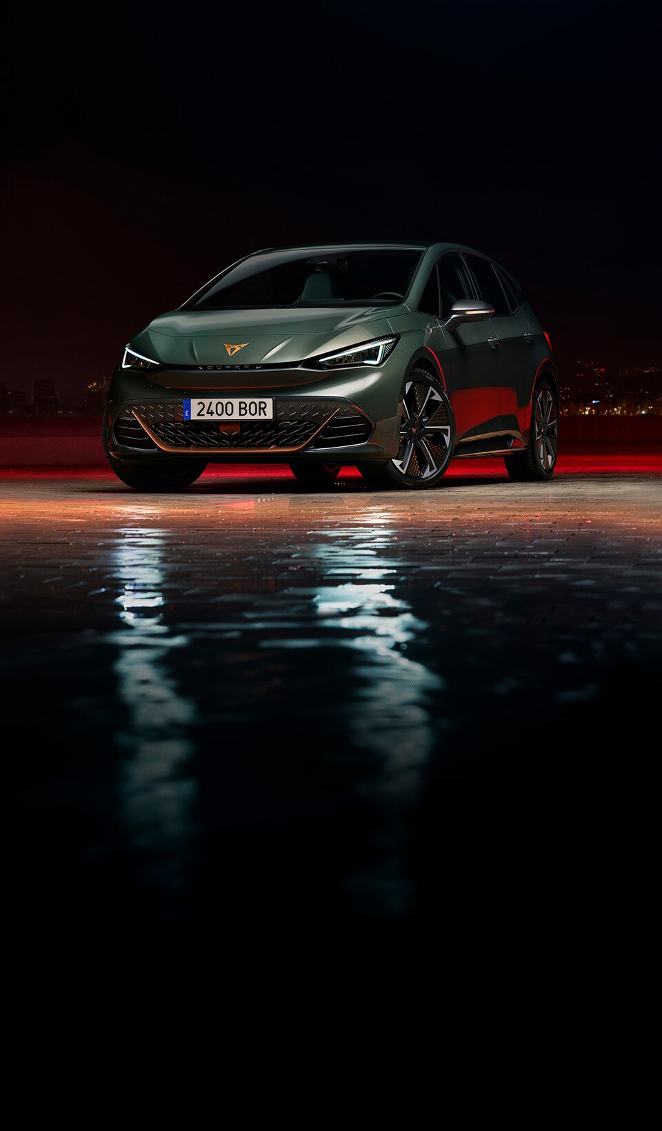 A CUPRA Formentor CUV suspended diagonally, next to a rocky, cliff-like structure. A charging cable is connected to the car from a charging unit on the cliff face.