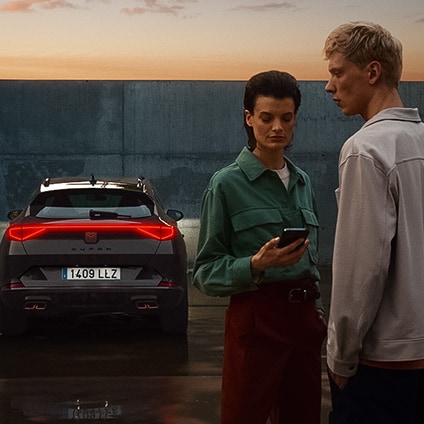 couple looking at purchasing options via phone, by cupra vehicle with rear lights on