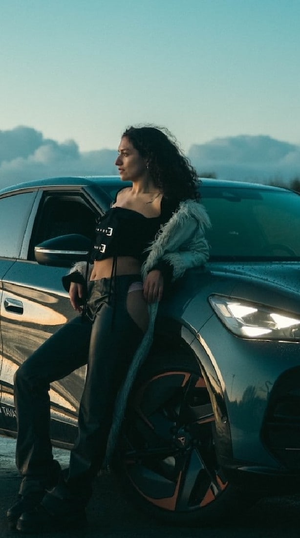 A minimalist image featuring a person wearing a dark hooded garment with subtle metallic details, against a black background.