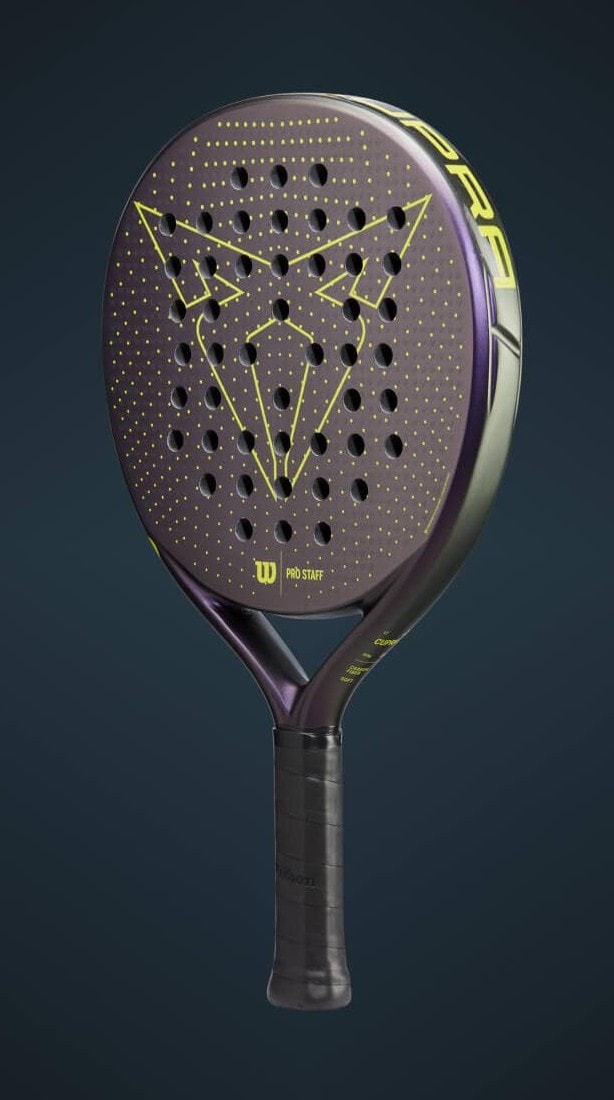 A padel court illuminated by blue lights, seen from above during a game within a large stadium filled with spectators. Two pairs of players are on the court and a large scoreboard is visible in the background.